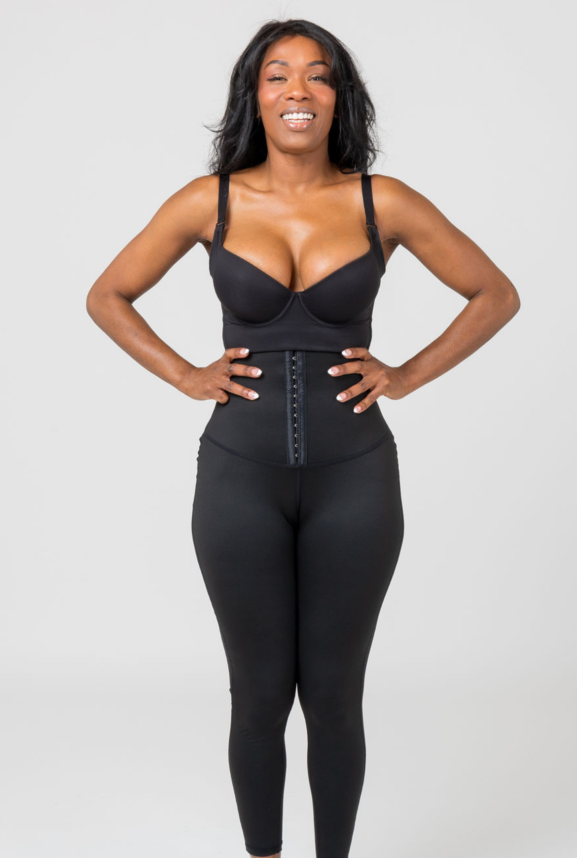 A person wearing a high-waisted black shapewear legging with adjustable straps.